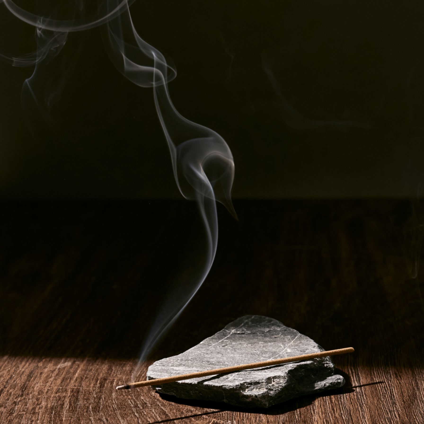 Incense stick on a rock with smoke against a dark background